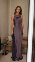 Front view of woman wearing dark purple satin cowl neck maxi dress with feather trim