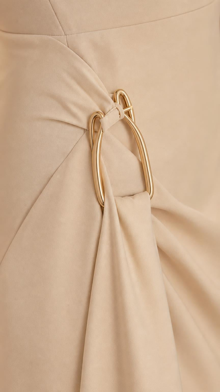 Close-up detail of gold-tone metallic ring accent and draped fabric on cream dress