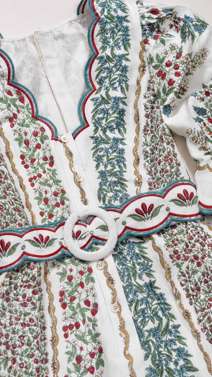 Close-up detail of embroidery, buttons, and belt on white romper