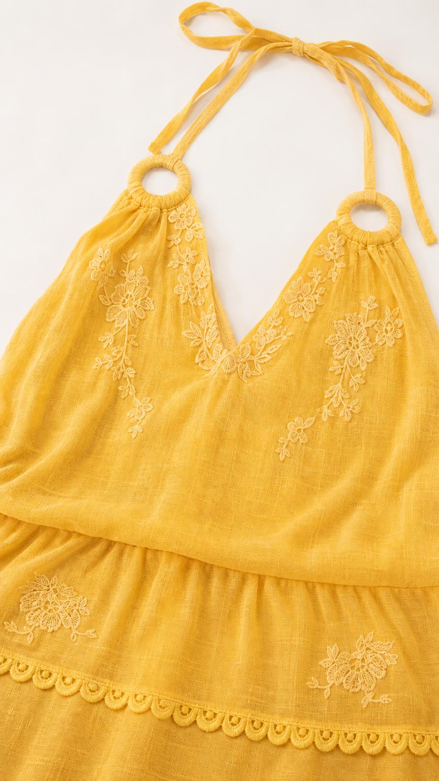 Close-up detail of yellow dress embroidery and halter neckline