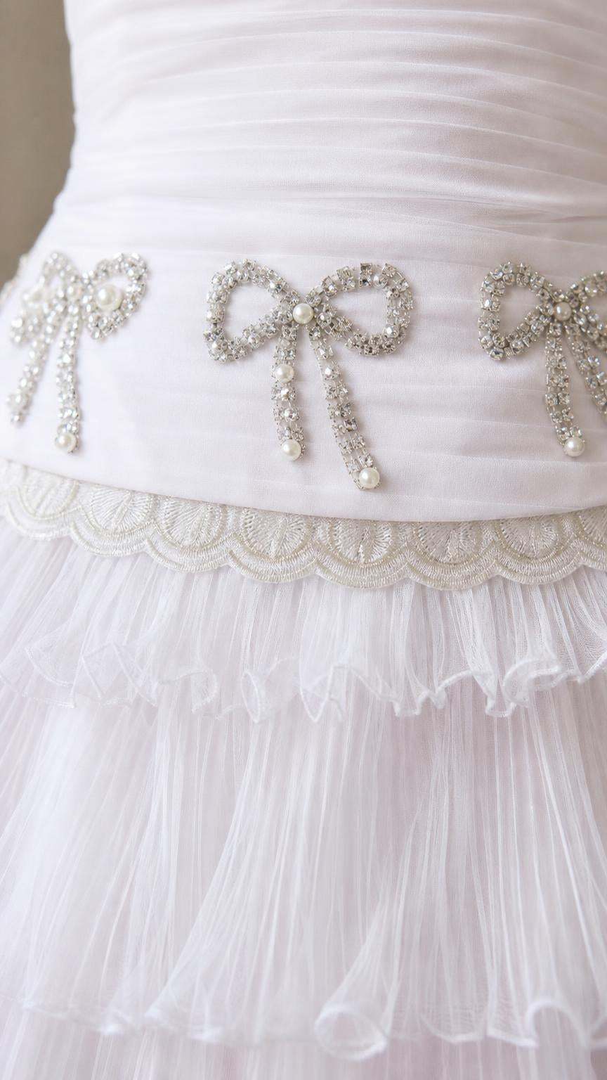 Close-up detail of rhinestone bow waist embellishment on white dress